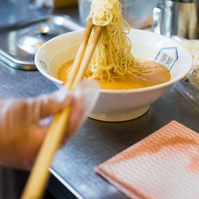 Kitchen image of RAKKAN RAMEN, mixing noodles and soup.