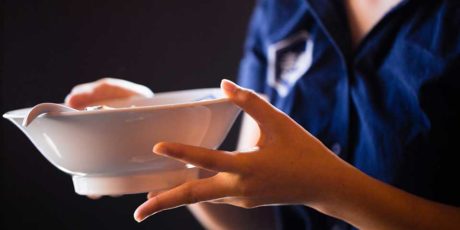 Kitchen image of RAKKAN RAMEN, a server is holding a ramen bowl.